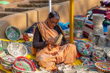 FARIDABAD, HARYANA / INDYA - Şubat 2020: Surajkund Craft Mela 'daki dükkanında el işi sepetleri ve maskeler takan yaşlı Hintli kadın