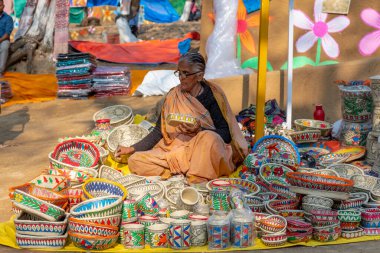 FARIDABAD, HARYANA / INDYA - Şubat 2020: Surajkund Craft Mela 'daki dükkanında el işi sepetleri ve maskeler takan yaşlı Hintli kadın