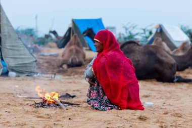 PUSHKAR, RAJASTHAN / INDIA - Kasım 2019: Pushkar Deve Fuarı Sahasında ısınmak için ateş püskürten etnik renkli rajasthani elbisesi içindeki Hintli kadının portresi
