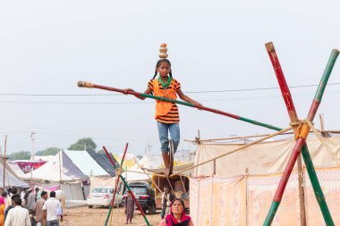 PUSHKAR, RAJASTHAN / INDIA - NOVEMBER 2019: Pushkar Fuarı 'nda sıkışık halatla akrobasi yapan ve bambuyla dengeyi sağlayan genç kız