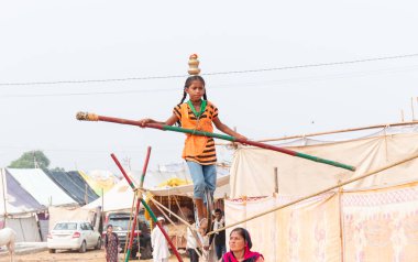 PUSHKAR, RAJASTHAN / INDIA - NOVEMBER 2019: Pushkar Fuarı 'nda sıkışık halatla akrobasi yapan ve bambuyla dengeyi sağlayan genç kız