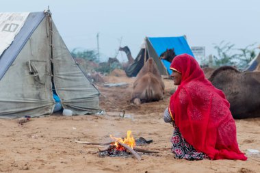 PUSHKAR, RAJASTHAN / INDIA - Kasım 2019: Pushkar Deve Fuarı Sahasında ısınmak için ateş püskürten etnik renkli rajasthani elbisesi içindeki Hintli kadının portresi
