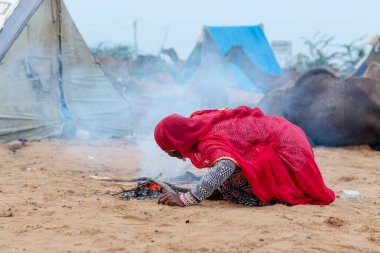 PUSHKAR, RAJASTHAN / INDIA - Kasım 2019: Pushkar Deve Fuarı Sahasında ısınmak için ateş püskürten etnik renkli rajasthani elbisesi içindeki Hintli kadının portresi