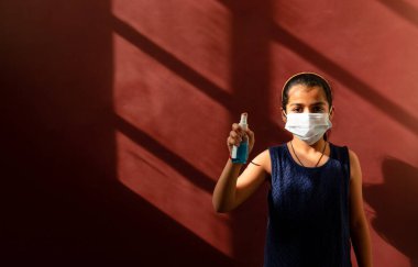 Yüzüne tıbbi maske takan genç kız virüsleri ve mikropları önlemek için dezenfektan kullanıyor. Renkli arkaplan kavramı.