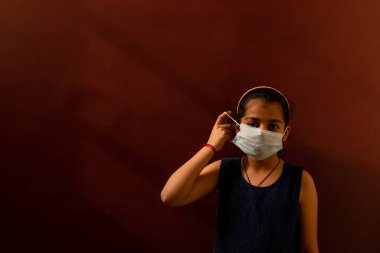 Yüzüne tıbbi maske takan genç kız virüsleri ve mikropları önlemek için dezenfektan kullanıyor. Renkli arkaplan kavramı.