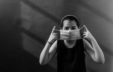 Yüzüne tıbbi maske takan genç kız virüsleri ve mikropları önlemek için dezenfektan kullanıyor. Renkli arkaplan kavramı.