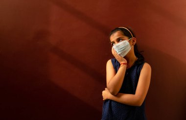 Yüzüne tıbbi maske takan genç kız virüsleri ve mikropları önlemek için dezenfektan kullanıyor. Renkli arkaplan kavramı.