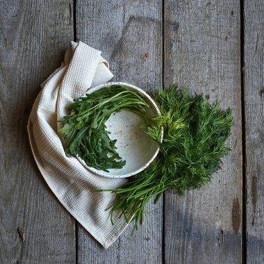 Arugula, beyaz peçete ve dereotlu ahşap arka planda yeşil roka ile siyah beyaz yuvarlak kasede. Gün ışığı. Yaklaş..
