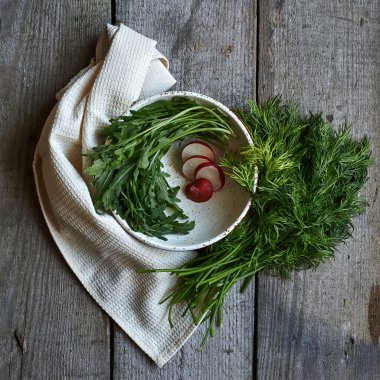 Beyaz peçete ve dereotlu, ahşap arka planda yeşil roka bulunan siyah beyaz yuvarlak kasede taze turp. Gün ışığı. Yaklaş..