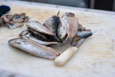 Beyaz kesme tahtasının üzerinde beyaz saplı bıçağın yanında yatan çok sayıda küçük balık.