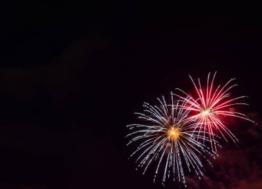 Two white with gold center starburst fireworks highlighted with red with a black background clipart