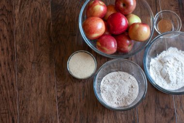 Elma, un, şeker, tarçın ve kahverengi şeker un karışımını içeren elmalı turta malzemeleri koyu ahşap arka plandaki bir grupta ayrı kaselerde konumlandırılmış.
