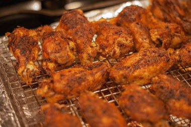 Close up of a metal rack full of home made chicken wings coming out of the oven using selective focus clipart