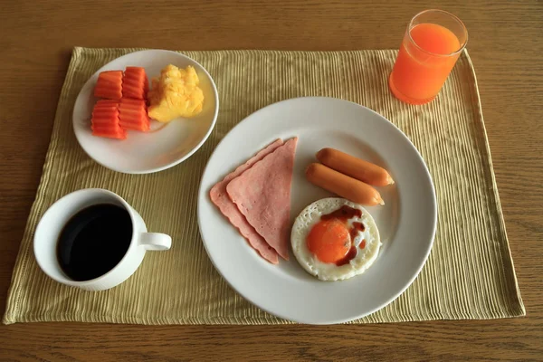 Conjunto de desayuno americano en mesa, huevo frito, jamón y salchicha con frutas frescas, jugo de naranja y café negro . — Foto de Stock