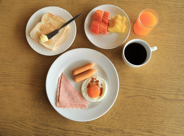 Conjunto de desayuno americano en mesa, huevo frito, jamón y salchichas, tostadas y mantequilla, frutas frescas, jugo de naranja y café negro . — Foto de Stock