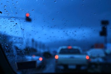 Araba penceresinden yağmur ile yol görünümünün soyut bulanık sahne düşer, mavi tonda renk, akşam bulutlu atmosferi.