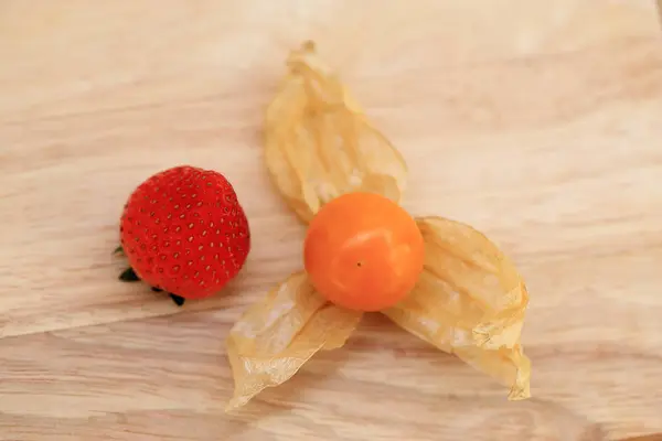 สตรอเบอร์รี่และผลไม้กูสเบอร์รี่เคปบนพื้นหลังไม้ . — ภาพถ่ายสต็อก