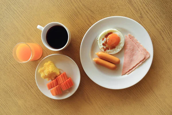 Σύνολο αμερικανικό πρωινό στο τραπέζι, τηγανητό αυγό, ζαμπόν και λουκάνικο με φρέσκα φρούτα, μαύρο καφέ, χυμό πορτοκάλι. — Φωτογραφία Αρχείου