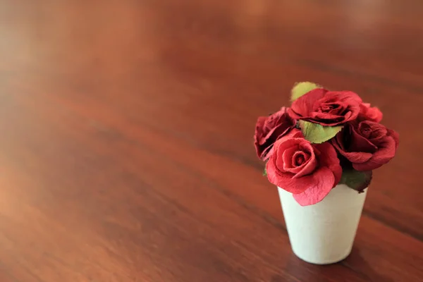 Red artificial roses in small white pot on wooden table with space for text. — Stock Photo, Image