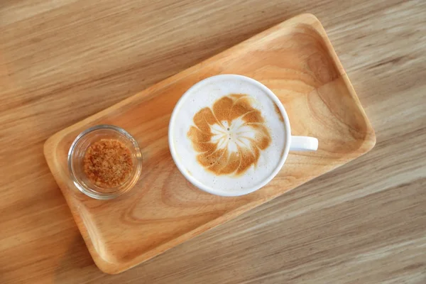 Sütlü latte sanat ve kahverengi şeker ahşap tepsi ile kahve fincan. — Stok fotoğraf