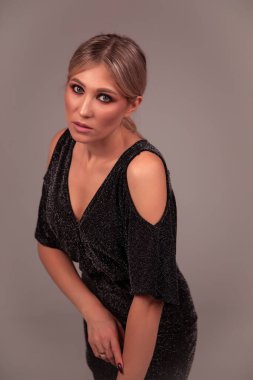 Stüdyoda zarif ve şık giyinmiş saçları, kırmızı dudakları ve dumanlı gözleri olan gülümseyen kadın poz veriyor.