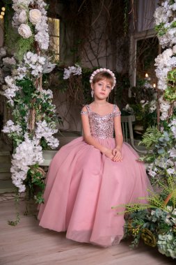 Pembe elbiseli küçük kız ve şapka sihirli çiçeklerin arasında oturuyor.