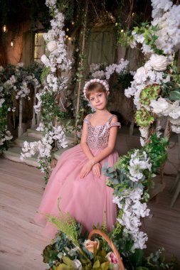 Pembe elbiseli küçük kız ve şapka sihirli çiçeklerin arasında oturuyor.