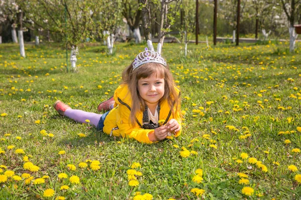 Little girl baby in yellow clothes lies on green grass and lots of dandelions