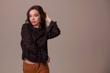 Güzel, genç seksi kız gülümseyip kahverengi bej arka planda poz veriyor. Boşluğu kopyala