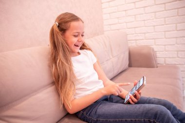 Küçük kız telefona bakıp gülümsüyor ve gülüyor. Teknoloji ve çocukluk