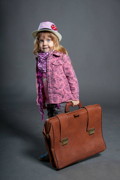 Little girl in hat holds big business suitcase for travel