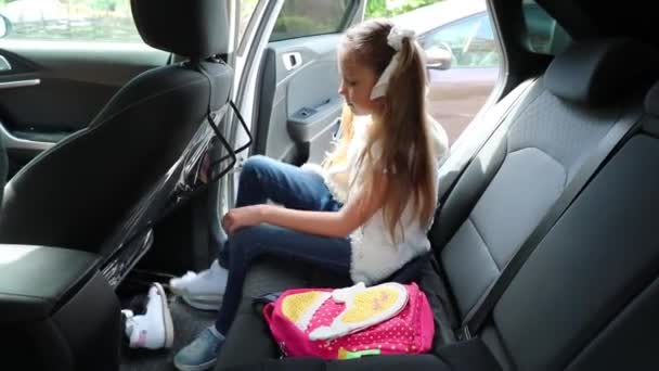 女の子は車の中で靴を履こうとする 子供はブーツを履き — ストック動画
