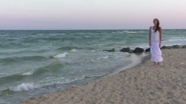 Beyaz giysili kadın sahil boyunca yürür