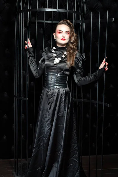 Jovem mulher de pé em um quarto escuro perto da gaiola . — Fotografia de Stock