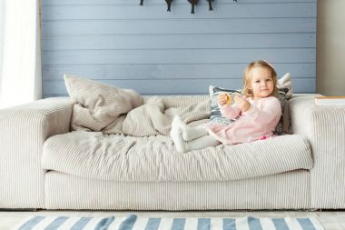 Küçük kız kanepede oturuyor.