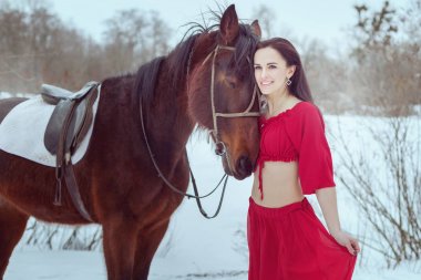 Esmer kadın kış orman at yanında duruyor.