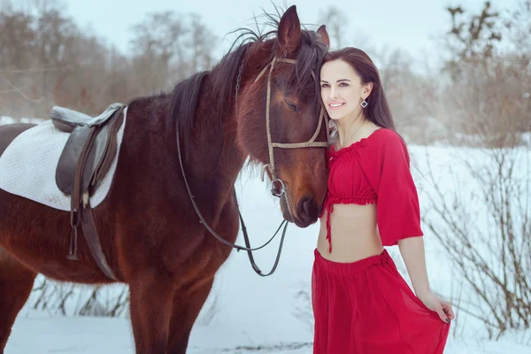 Esmer kadın kış orman at yanında duruyor.