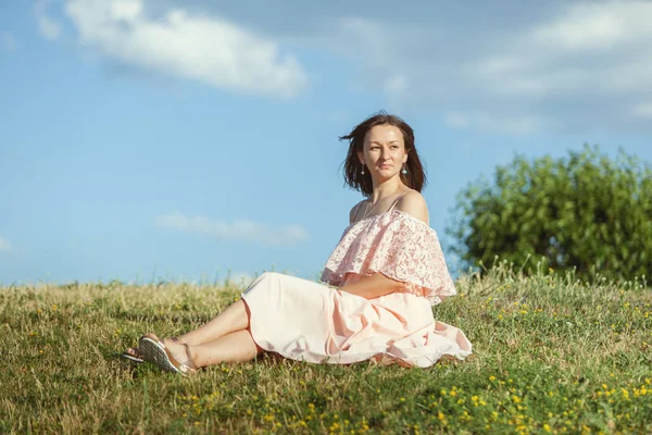 Kvinna i en klänning sitter på gräset. — Stockfoto