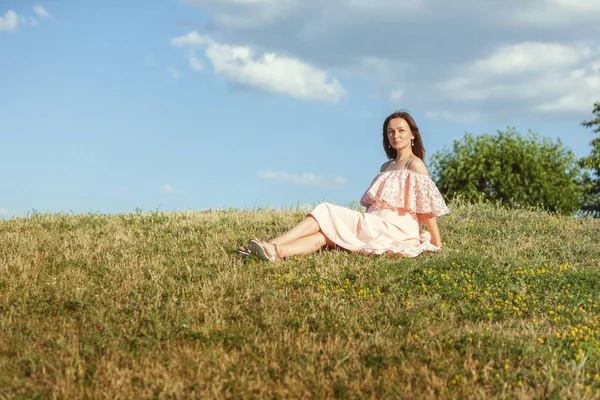 Brunetka Kobieta w sukni siedzi na trawie. — Zdjęcie stockowe