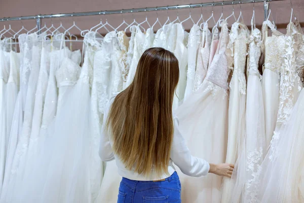 Vacker kvinna i en bröllopssalong tittar på brudklänningar. — Stockfoto