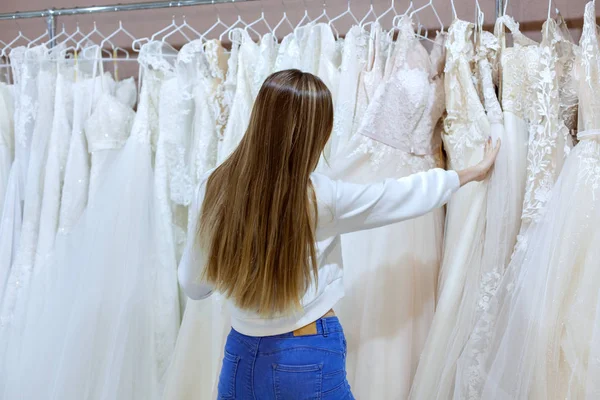 Jovem mulher em um salão de casamento olha para vestidos de noiva . — Fotografia de Stock