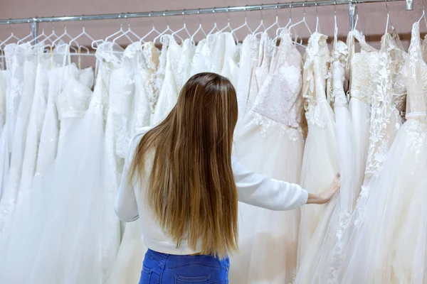 Mulher bonita em uma boutique de casamento olha para vestidos de noiva . — Fotografia de Stock