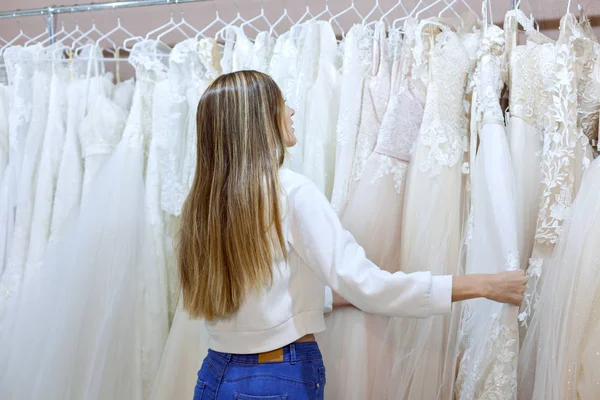 Ung kvinna i en bröllopsbutik tittar på brudklänningar. — Stockfoto