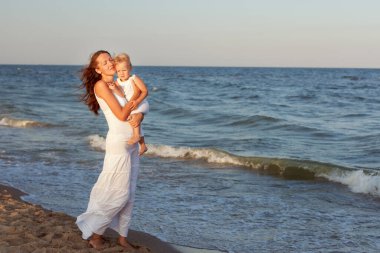 Genç anne ve kızı kumlu deniz kıyısında yürüyorlar..