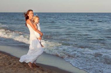 Genç anne ve kızı deniz kenarında yürüyor..