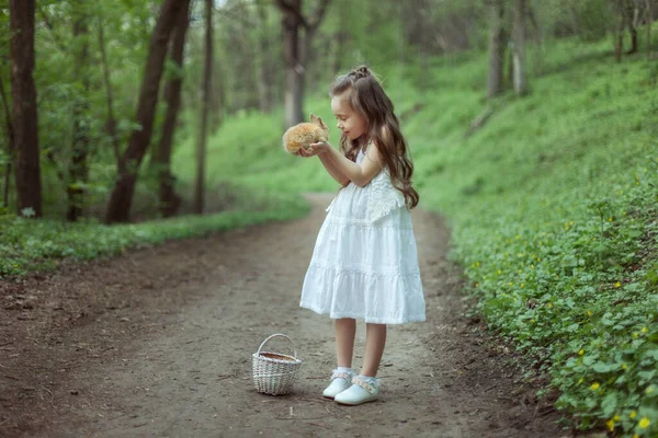 愛らしい赤ちゃんが森の中を歩く 彼女は手にウサギを持っている — ストック写真