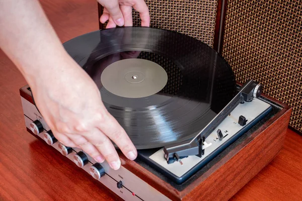 Hands put a vinyl on an old wooden turntable