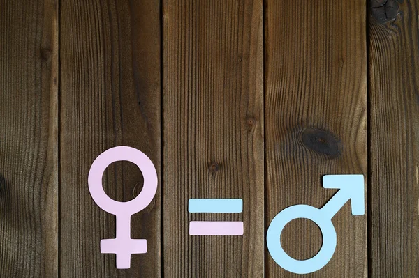 male and female symbols cut out of paper and an equal sign on a wooden background. the concept of gender equality. space for text