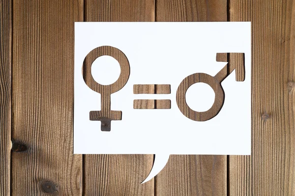 male and female symbols and an equal sign in white dialogue box cut out of paper on a wooden background. the concept of gender equality