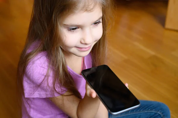 little six year old girl using a smartphone voice recognition online sitting on floor at home. noise